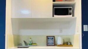 A compact kitchen with white cabinets, a microwave, and a small shelf with books and a flag. - Westminster Mount View Unit 1 (Rotorua)