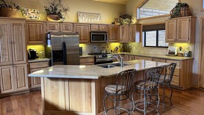 Un'ampia cucina con mobili in legno, una grande isola con sgabelli da bar, elettrodomestici in acciaio inossidabile e un cartello con scritto 'Thankful & Blessed'.
