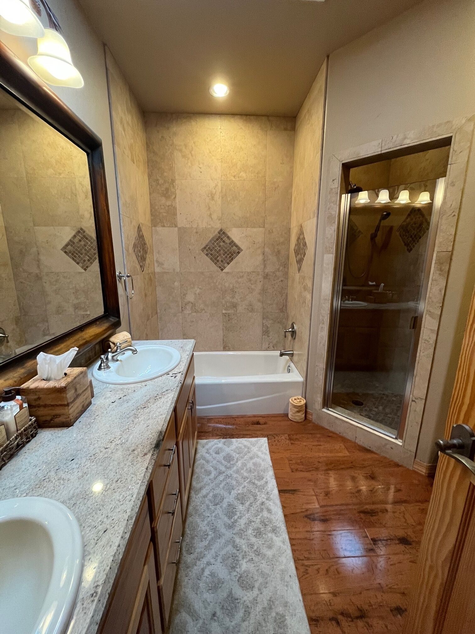 A bathroom with a double sink, a bathtub, a glass-enclosed shower, and a wooden vanity.