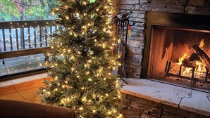 Un accogliente soggiorno con un albero di Natale illuminato, un camino in pietra e vista sugli alberi.
