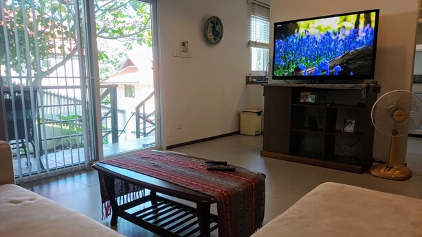 Ett vardagsrum med en soffa, ett soffbord, en tv på ett tv-bord, en fläkt och utsikt över en balkong med ett räcke.
