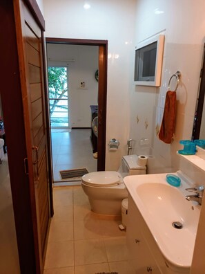 A bathroom with a toilet, sink, and a mirror. There is a door leading to another room. - Peaceful 1 BR home in private residence (Koh Samui)
