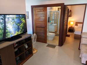 A hotel room with a television, a fan, a wooden door leading to a bathroom, and a bed. - Peaceful 1 BR home in private residence (Koh Samui)