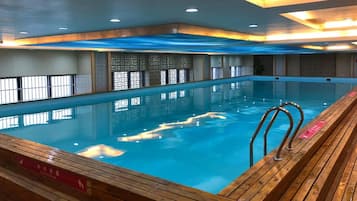 An indoor swimming pool with wooden deck and safety railings.