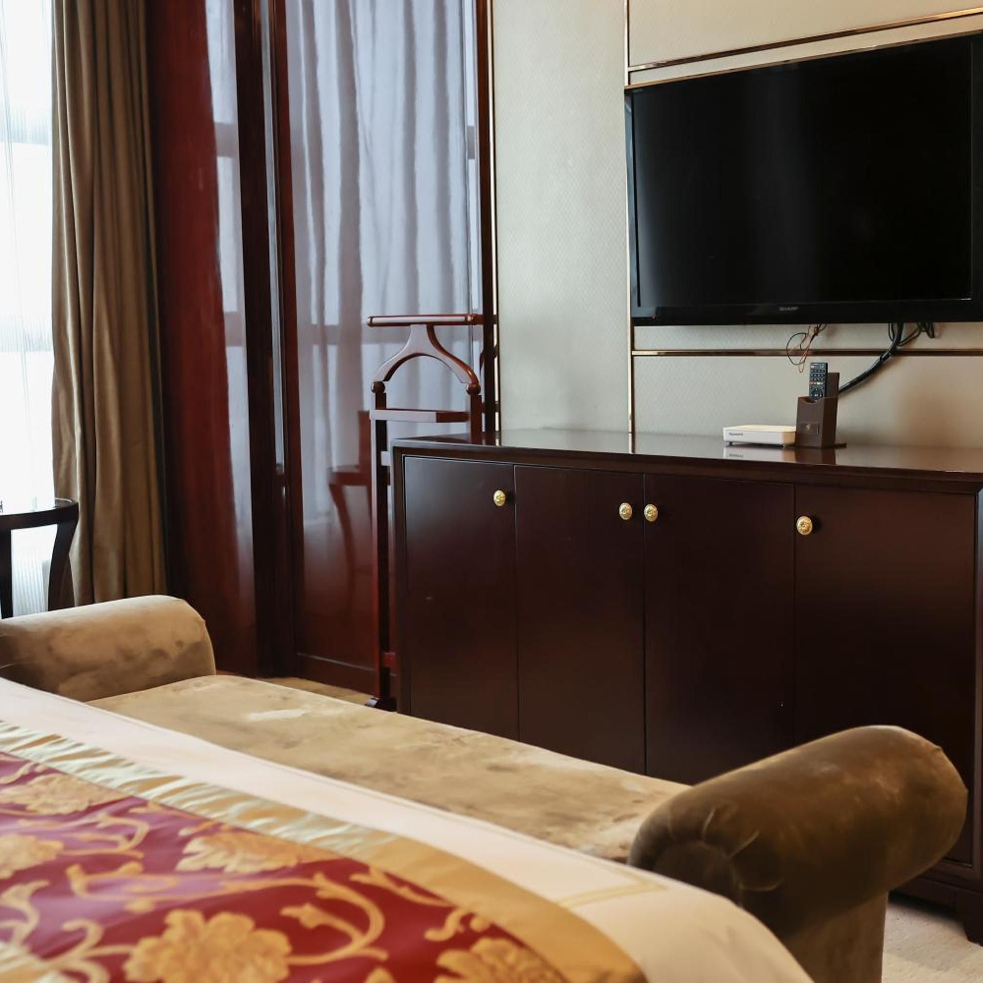Una habitación de hotel con una cama, un televisor montado en la pared y un aparador de madera.