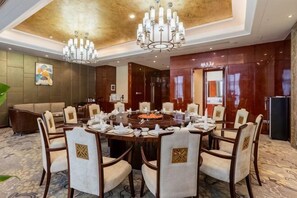 Un salón de conferencias con una mesa redonda, sillas, candelabros y un cuadro grande en la pared.