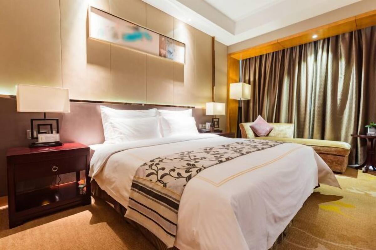 Ein Hotelzimmer mit Bett, Nachttischen, einer Lampe, einem Wandregal und einem Vorhang.