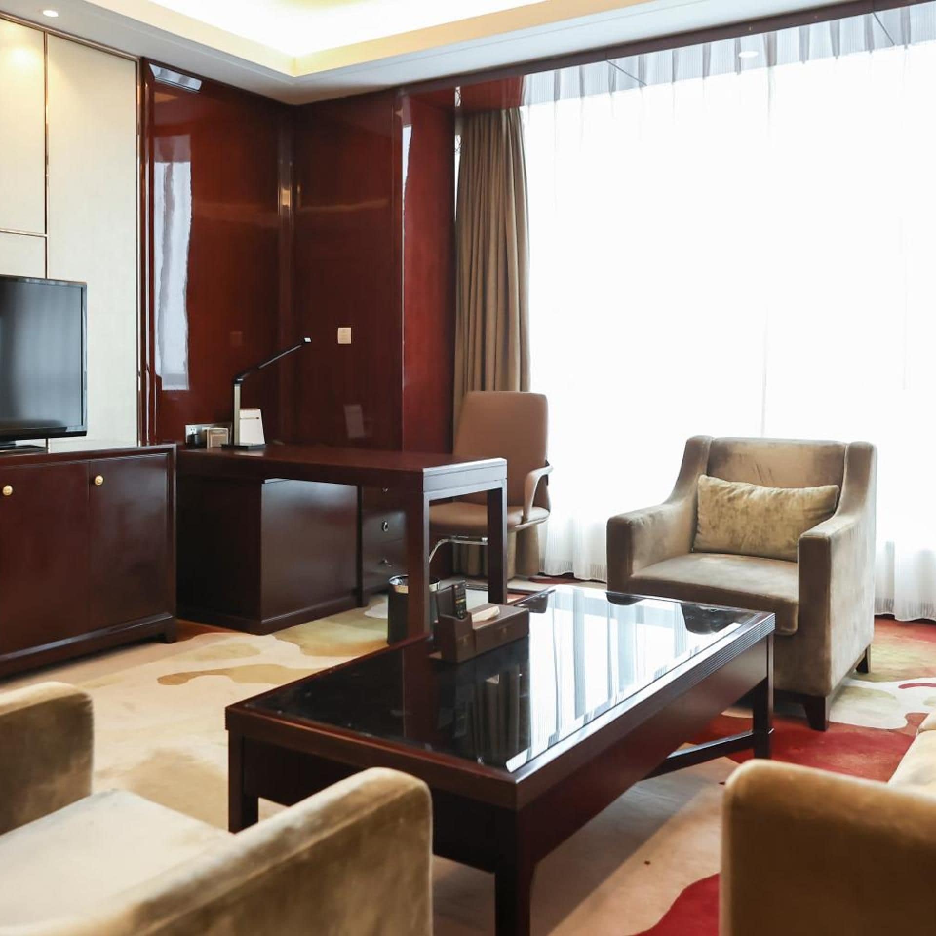 Ein Hotelzimmer mit einem großen Flachbildfernseher, einem Holztisch, einem Ledersessel, einer Couch und einem Glastisch.