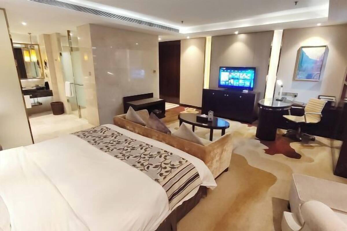 Ein Hotelzimmer mit einem großen Bett, einem Schreibtisch mit Stuhl, einem Fernseher und einem Badezimmer mit Spiegel und Waschbecken.
