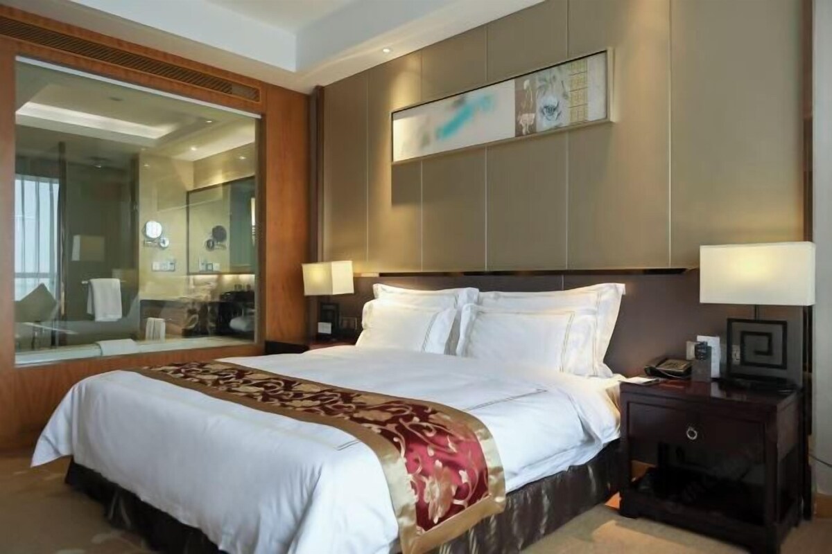 Une chambre d’hôtel avec un grand lit, un miroir, une table de chevet et une œuvre d’art accrochée au mur.