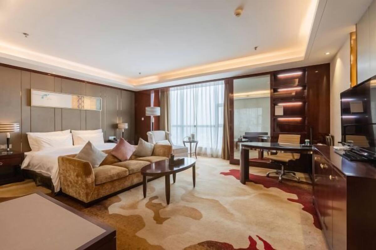 Ein modernes Hotelzimmer mit einem großen Bett, einer Couch, einem Schreibtisch und einem Fernseher.
