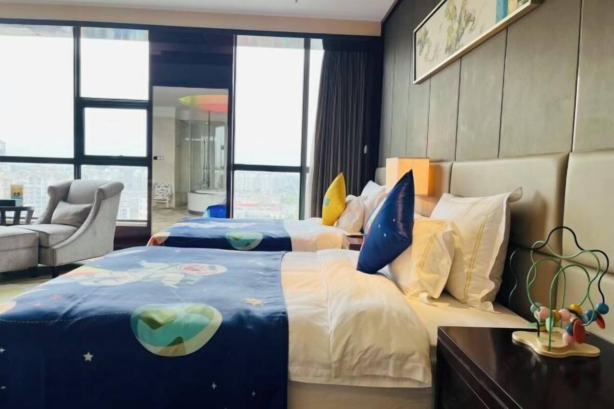Ein Hotelzimmer mit zwei Betten, einer Couch und Blick auf die Stadt, inklusive großem Fenster.
