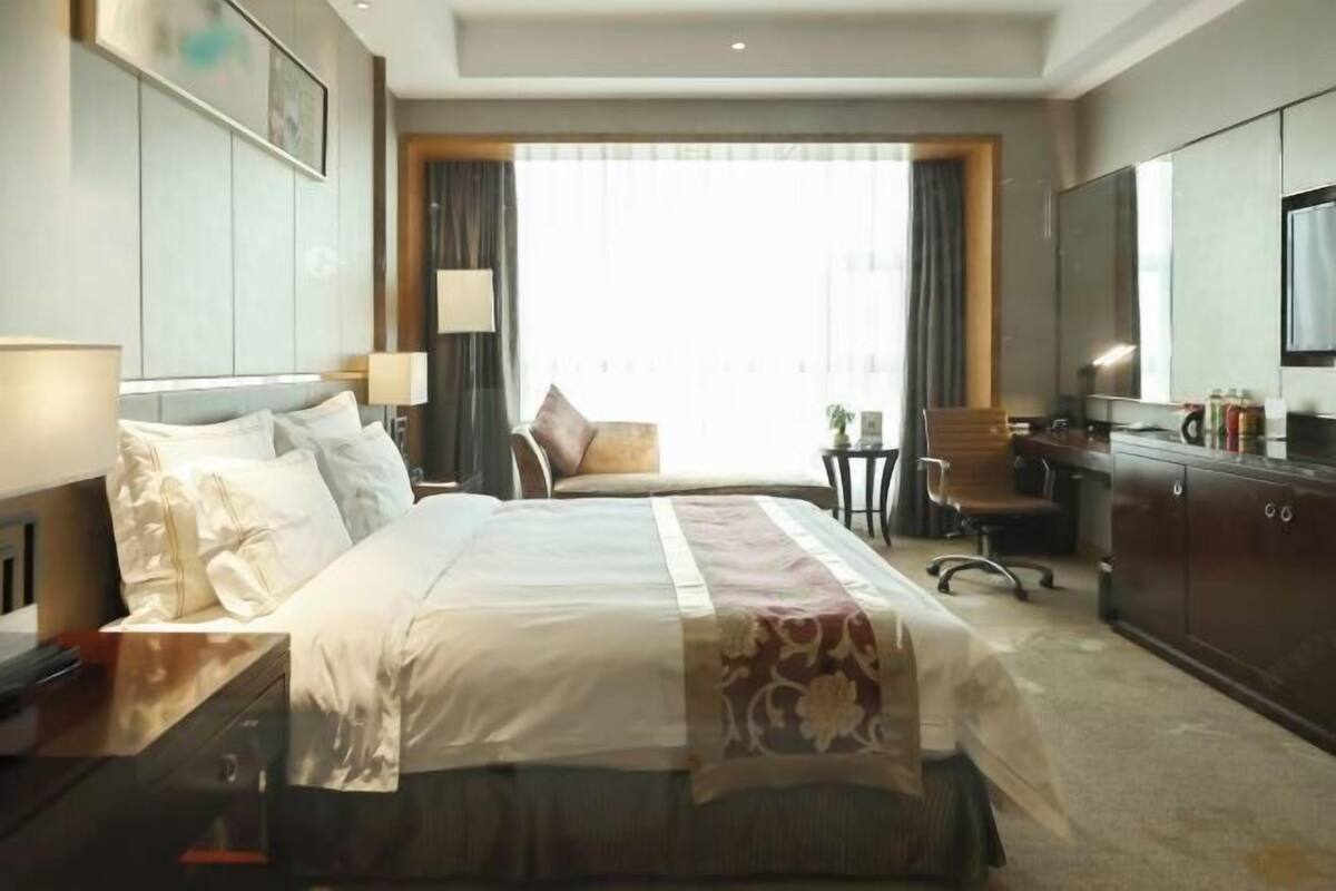 Ein Hotelzimmer mit einem großen Bett, einem Schreibtisch, einem Sessel, einem Fernseher und einem Kleiderschrank.