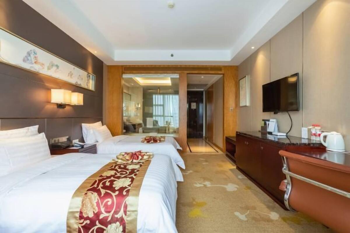 Ein Hotelzimmer mit zwei Betten, einem Holzschrank, einem Fernseher und einem Spiegel.