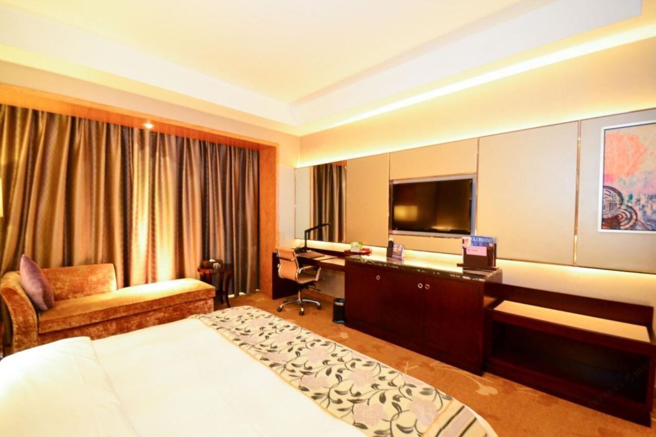 A hotel room with a bed, a desk, a chair, a television, and a large window with curtains.