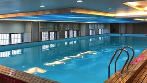 En inomhuspool med ett trädäck, kaklade väggar och ett tak med infälld belysning.