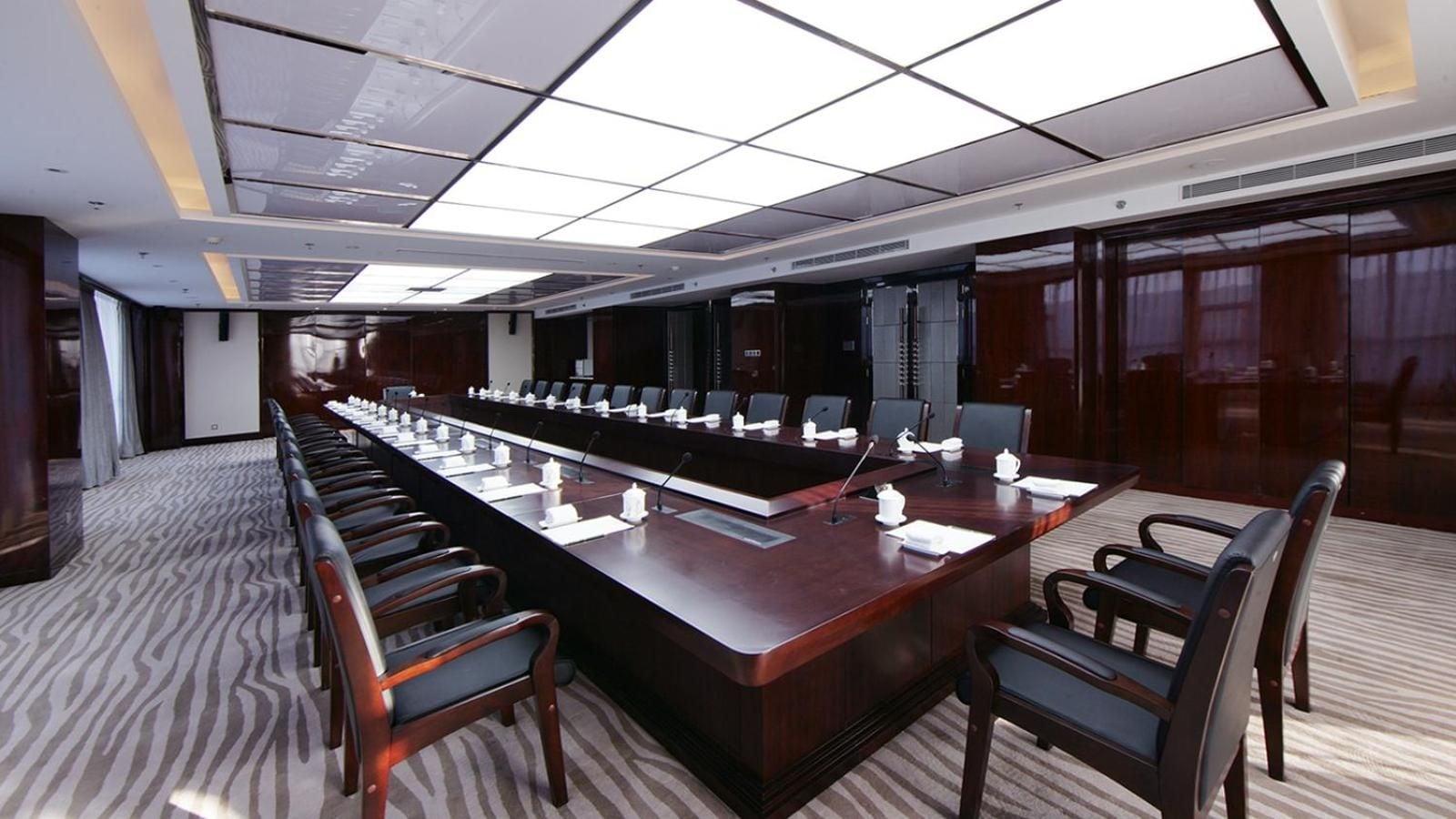A conference room with a long table, chairs, microphones, and nameplates.