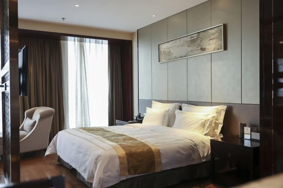 Ein modernes Hotelzimmer mit einem großen Bett, einem Sessel, einem Flachbildfernseher und einem Bild an der Wand.