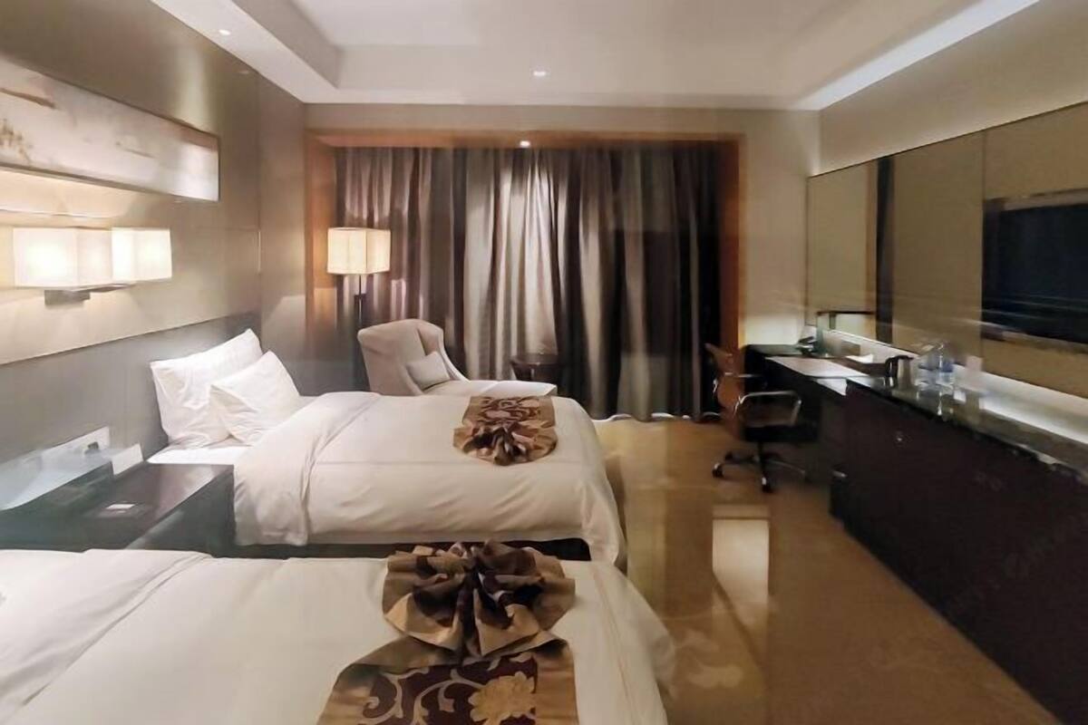 Ein Hotelzimmer mit zwei Betten, einem Schreibtisch, einem Stuhl, einem Fernseher und einem großen Fenster mit Vorhängen.
