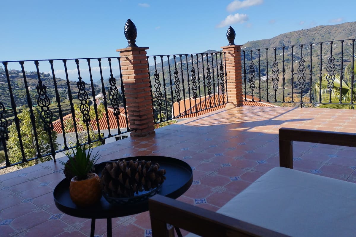 Une terrasse offrant une vue sur un paysage vallonné, avec un sol carrelé et une rambarde en métal.