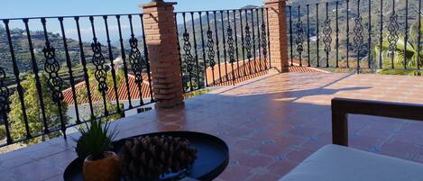 A terrace with a view of a hilly landscape, featuring a tiled floor and a metal railing.