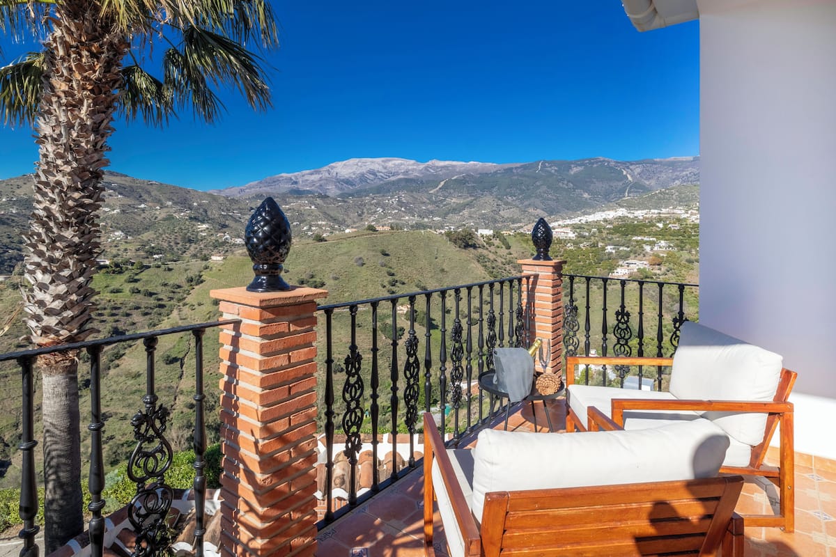 Un balcon avec une chaise en bois et une table, donnant sur un paysage montagneux.