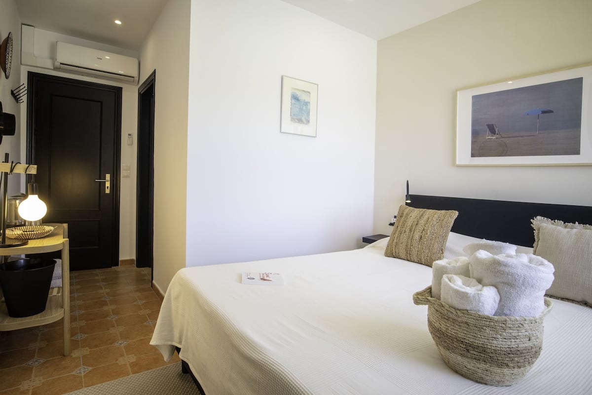 Une chambre d’hôtel avec un lit, un panier rempli de serviettes, un tableau encadré au mur et un appareil de climatisation.