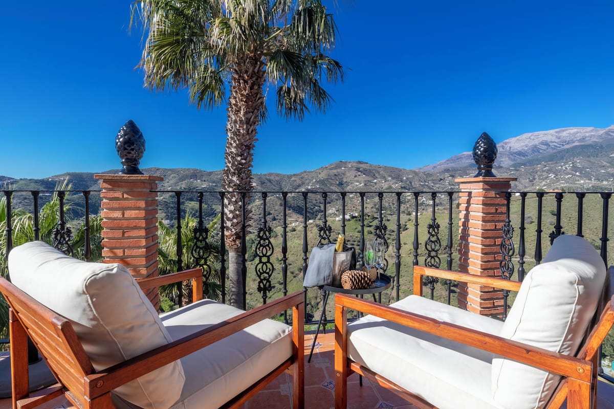 Un balcon avec deux chaises en bois et une petite table, donnant sur un paysage montagneux.