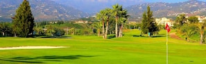 A golf course with a flag, palm trees, and a distant mountain range. - Malaga Hills, Adults Only boutique, wellness & hiking Eco-Hotel (Còmpeta)