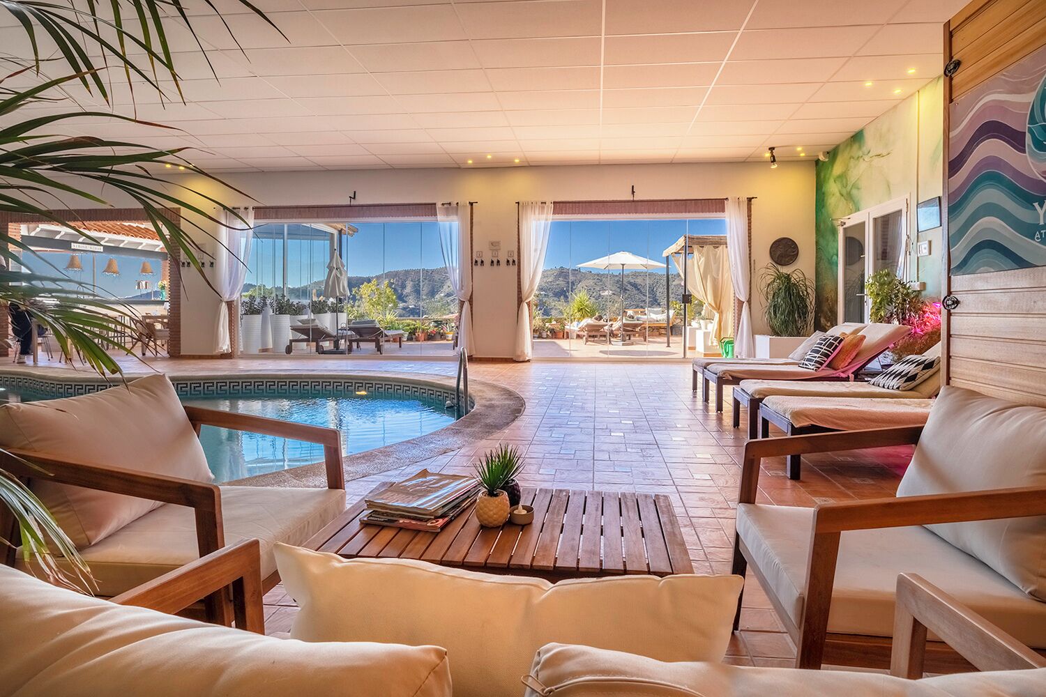 Zona de piscina con sillones de descanso, una mesa de madera y vistas a la piscina.