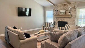 Una sala de estar con televisor de pantalla plana montado en la pared, chimenea con revestimiento de piedra y un sofá modular grande.