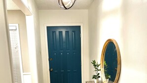 Un pasillo con una puerta azul, una consola de madera con un espejo y una lámpara colgante.