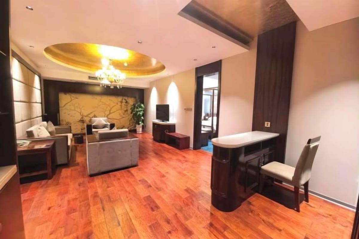 A spacious living area with a wooden floor, a sofa, a dining table with chairs, and a TV.