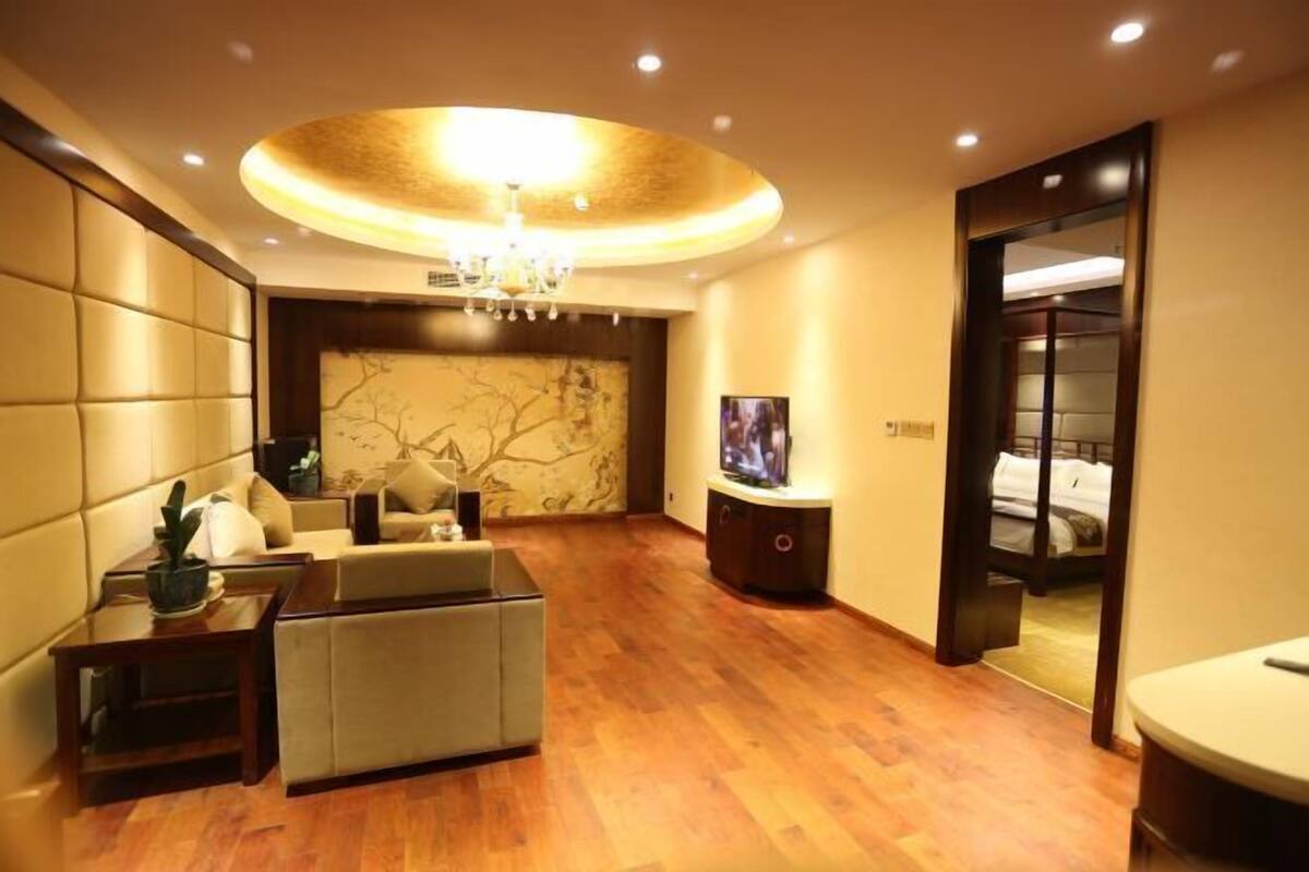 A modern hotel room with a wooden floor, a sofa, a TV, and a large mirror.