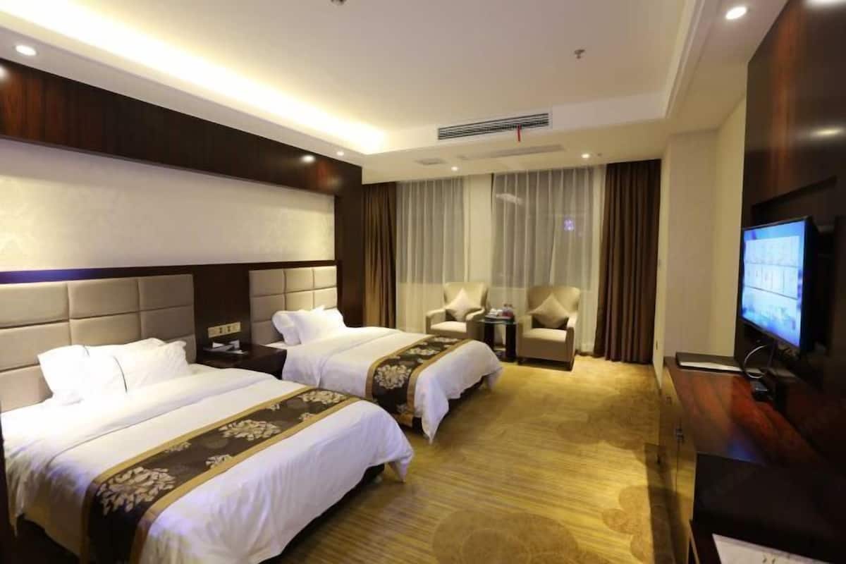 A hotel room with two beds, a TV, a sofa, and a small table.