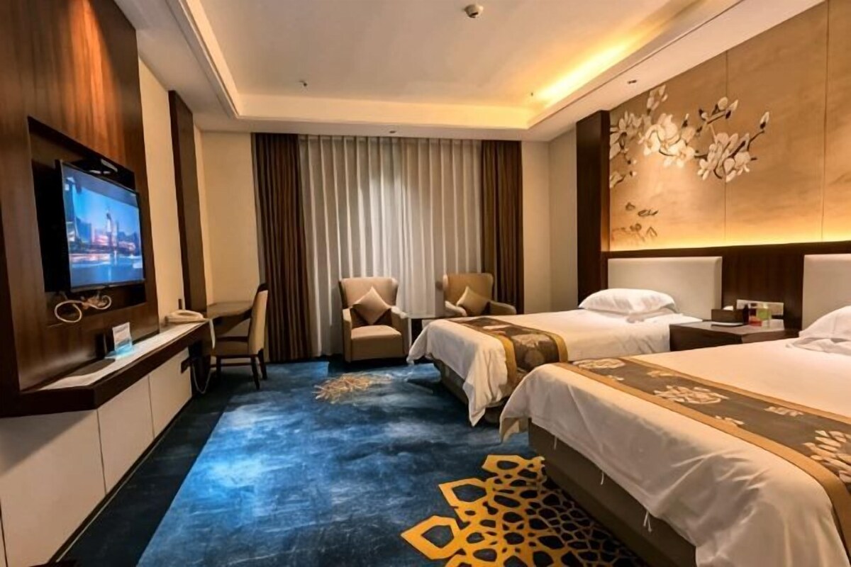 A hotel room with a bed, a desk with a TV, a chair, and a wall-mounted TV.