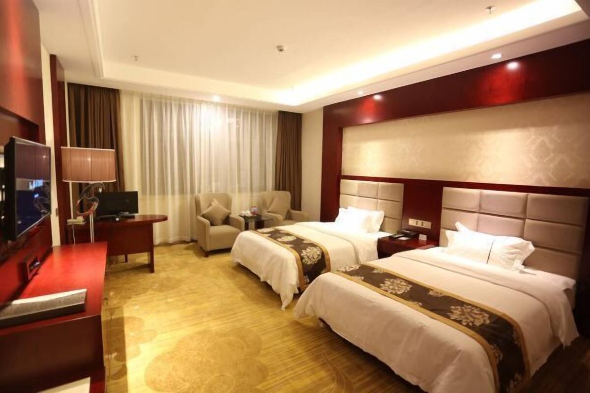 A hotel room with two beds, a TV, a desk, and a chair.