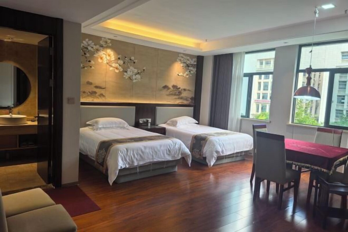 A hotel room with two beds, a dining table, and a large window.
