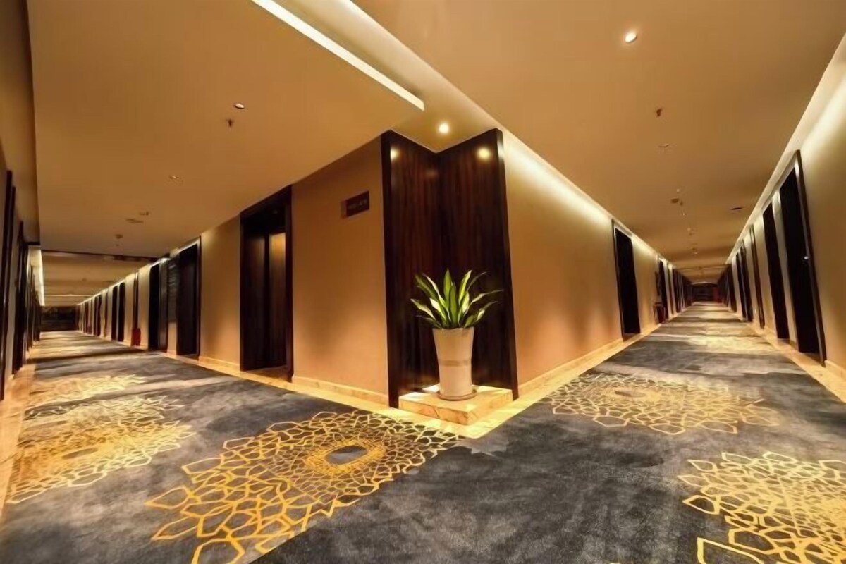 A hotel corridor with a carpeted floor, a potted plant, and doors on both sides.