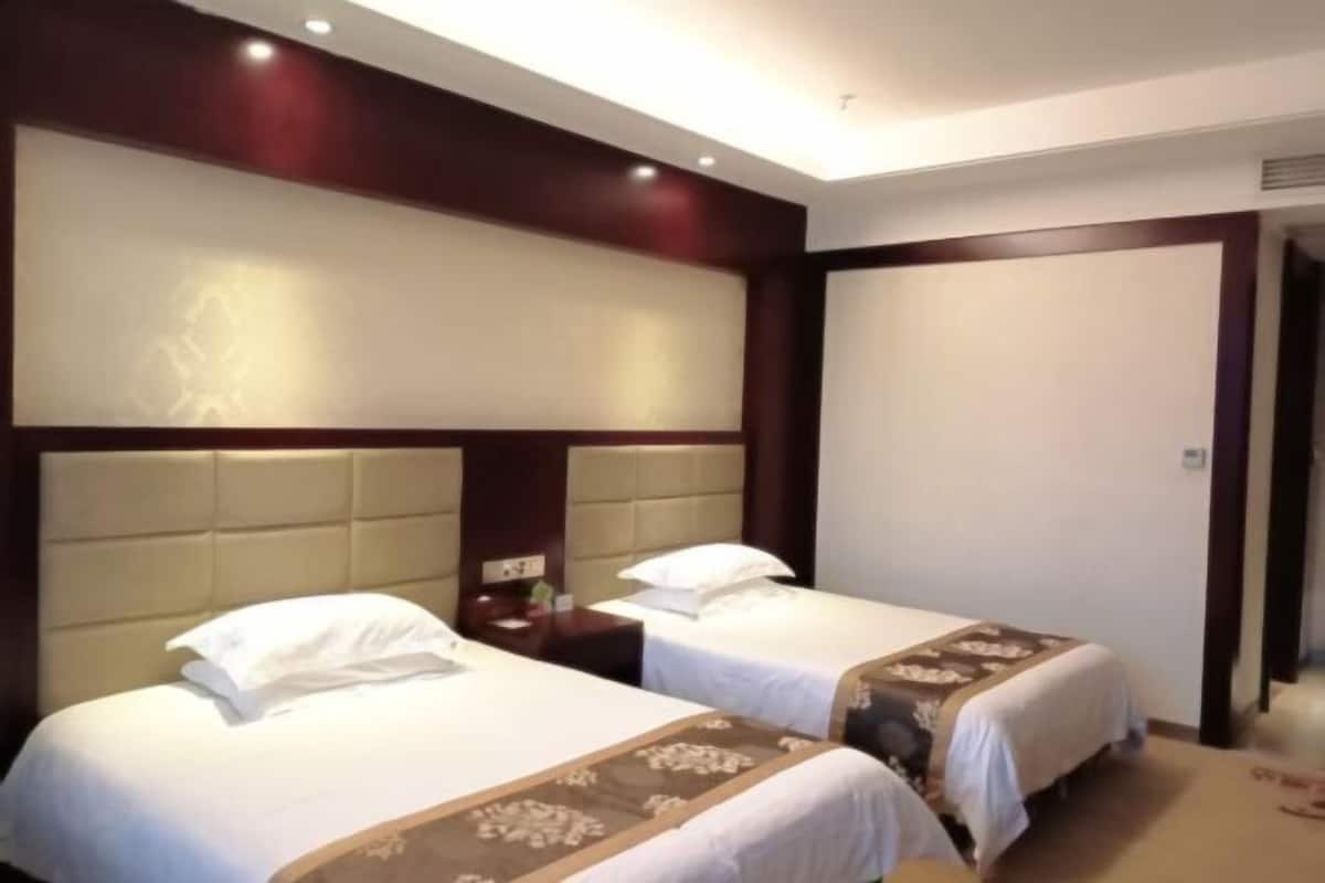 A hotel room with two beds, each with a headboard and white bedding.