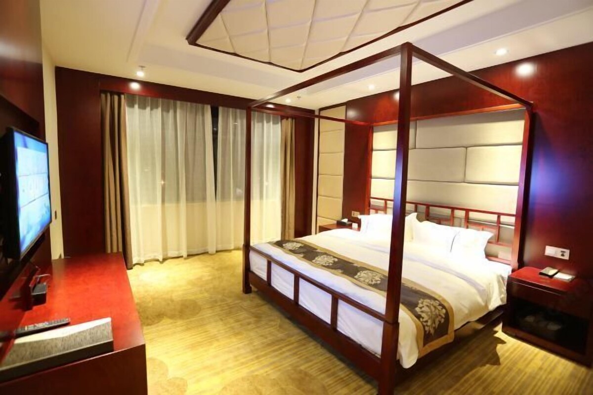 A four-poster bed with a headboard, a television on a stand, and a bedside table with a lamp.
