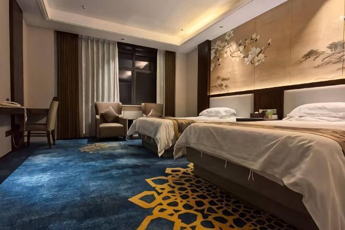 A hotel room with a bed, a desk, a chair, and a large window.