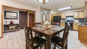 Un comedor con mesa y sillas de madera, una araña y una cocina con armarios y electrodomésticos de madera.