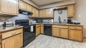 Una cocina con armarios de madera, estufa negra, microondas y lavavajillas.