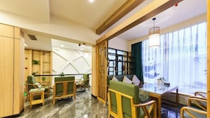 Een moderne hotel lobby met een marmeren vloer, houten meubels, een groene bank en een eetgedeelte met een glazen tafel.