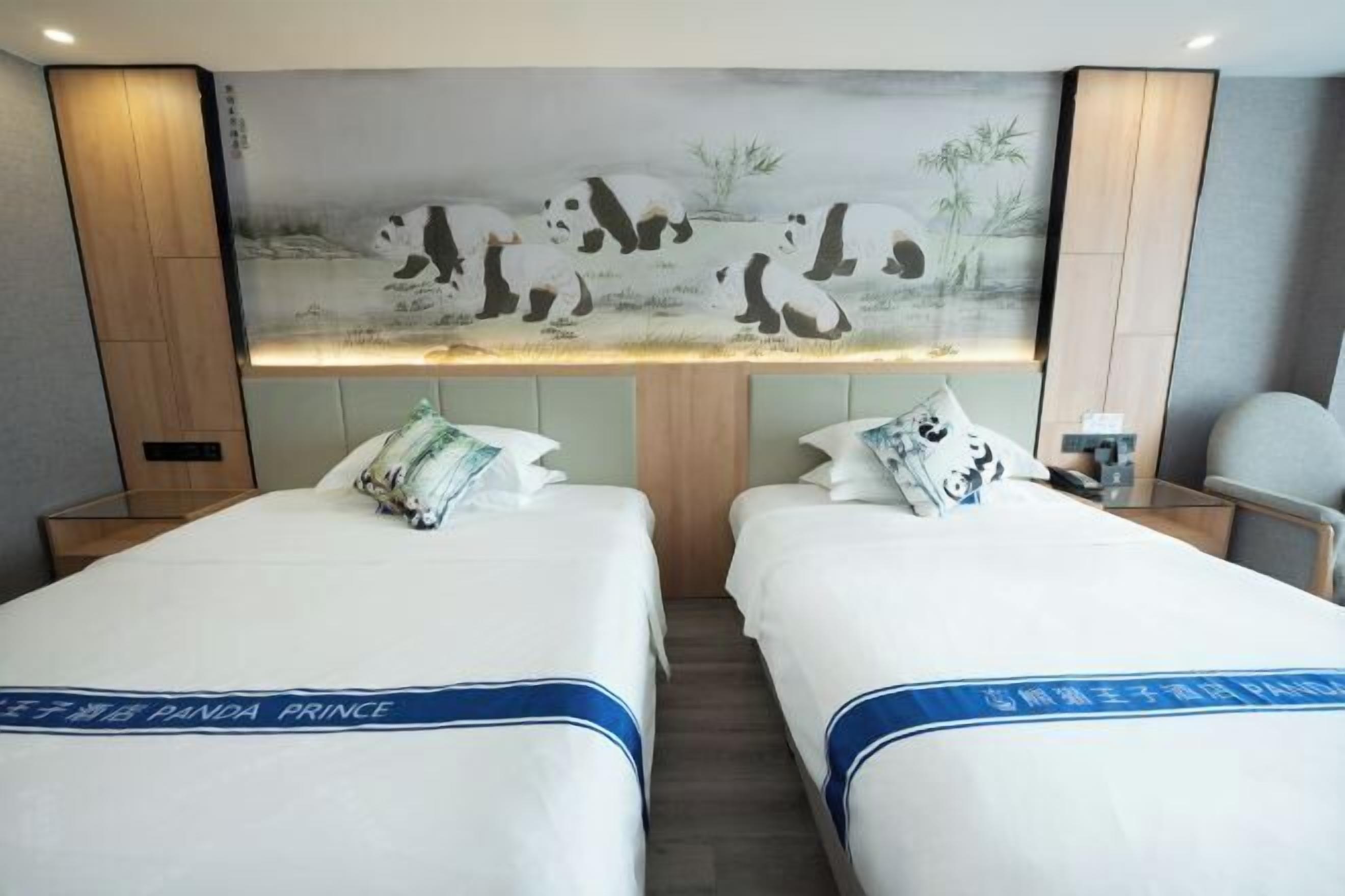 A hotel room with two beds, a panda-themed mural, and a nightstand with a lamp.
