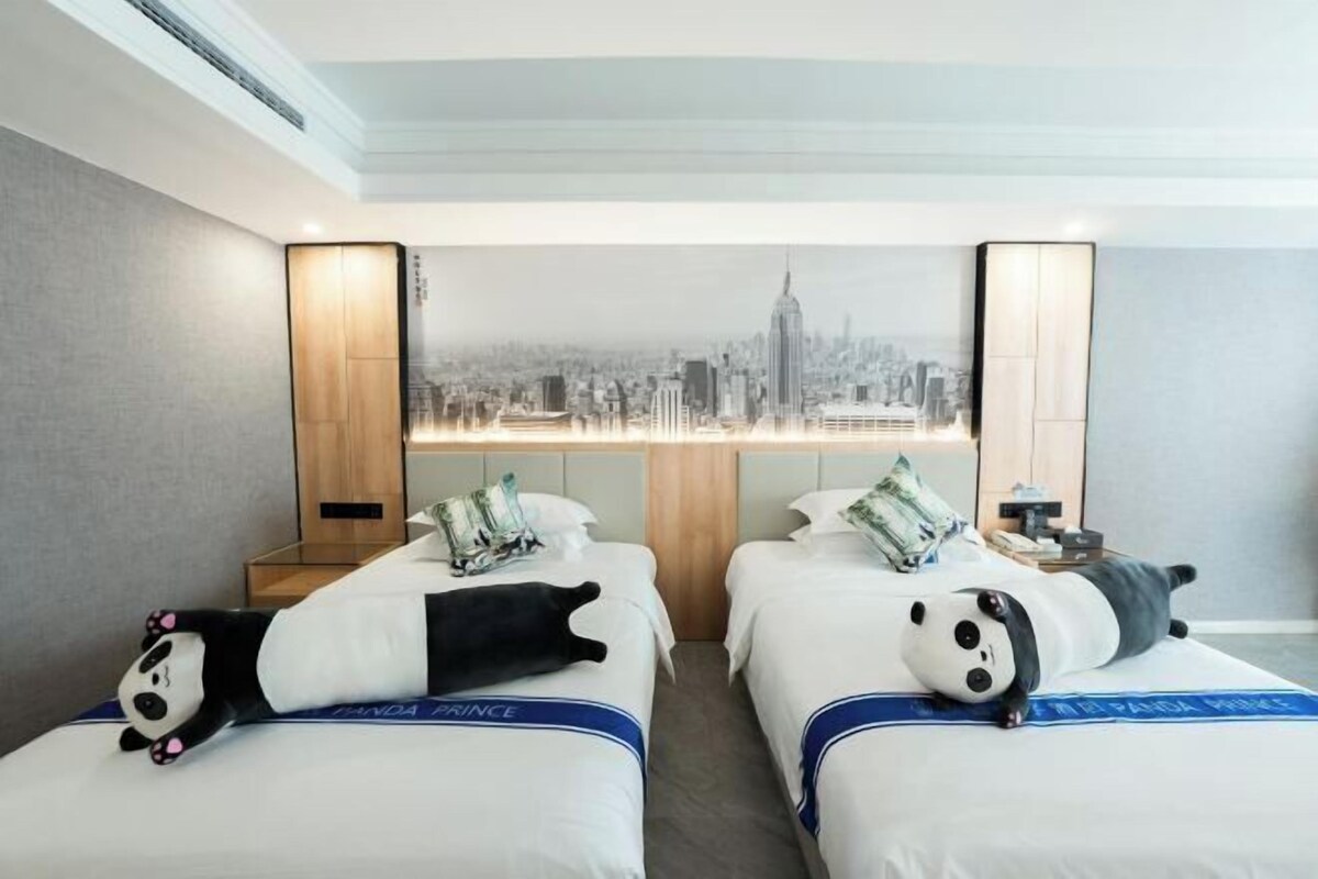 A hotel room with two beds, each with a cityscape view and a panda-themed pillow.