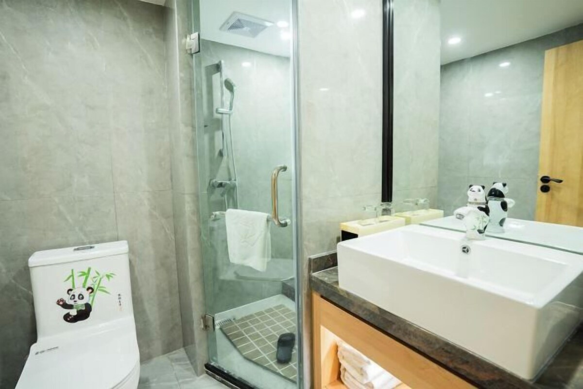 A modern bathroom with a glass shower enclosure, a large sink, and a toilet with a panda decal.