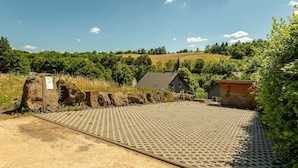 A parking area with a gravel surface and a paved walkway leading to a building with a sloped roof.