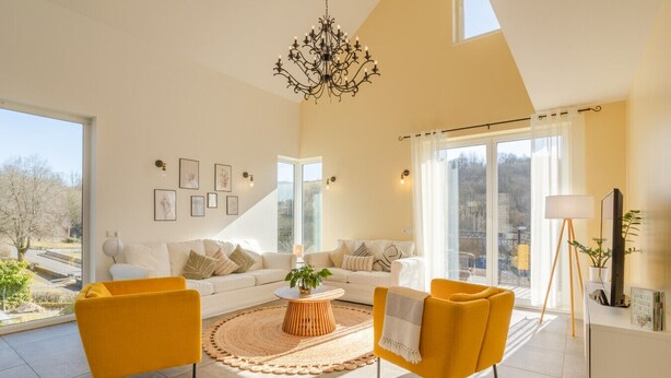 A spacious living room with a high ceiling, large windows, and a chandelier.